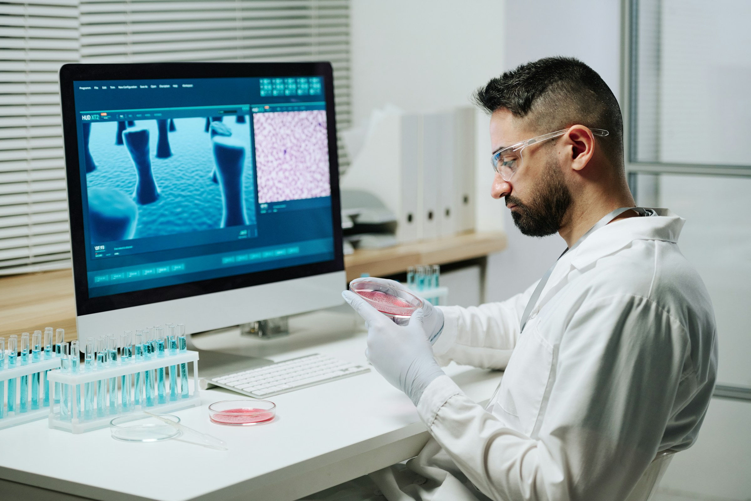 Scientist in a white lab coat analyzing microscopic images on a computer screen in a laboratory.